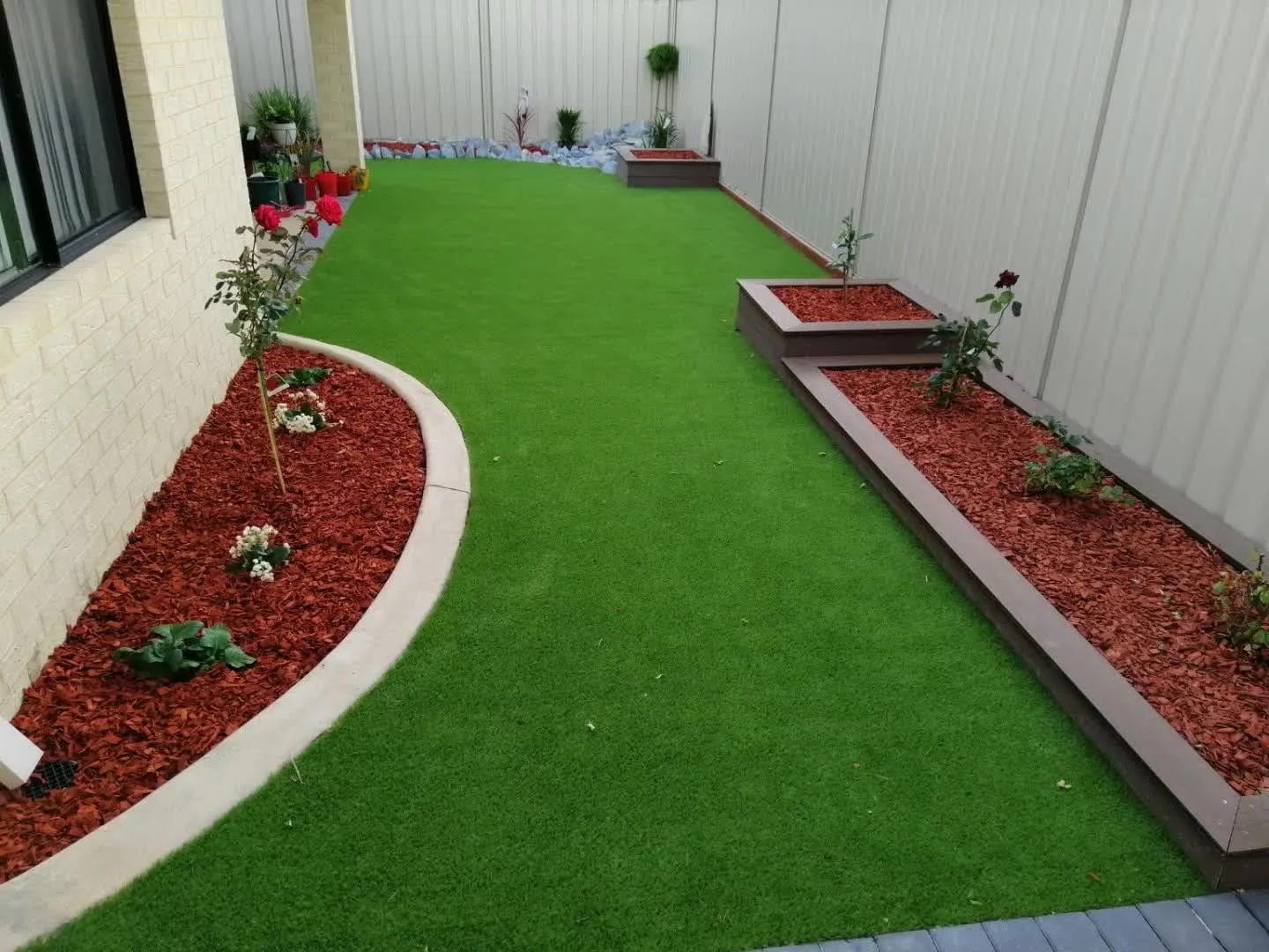 Artificial grass lawn framed by curved red-mulch garden beds and retaining edging
