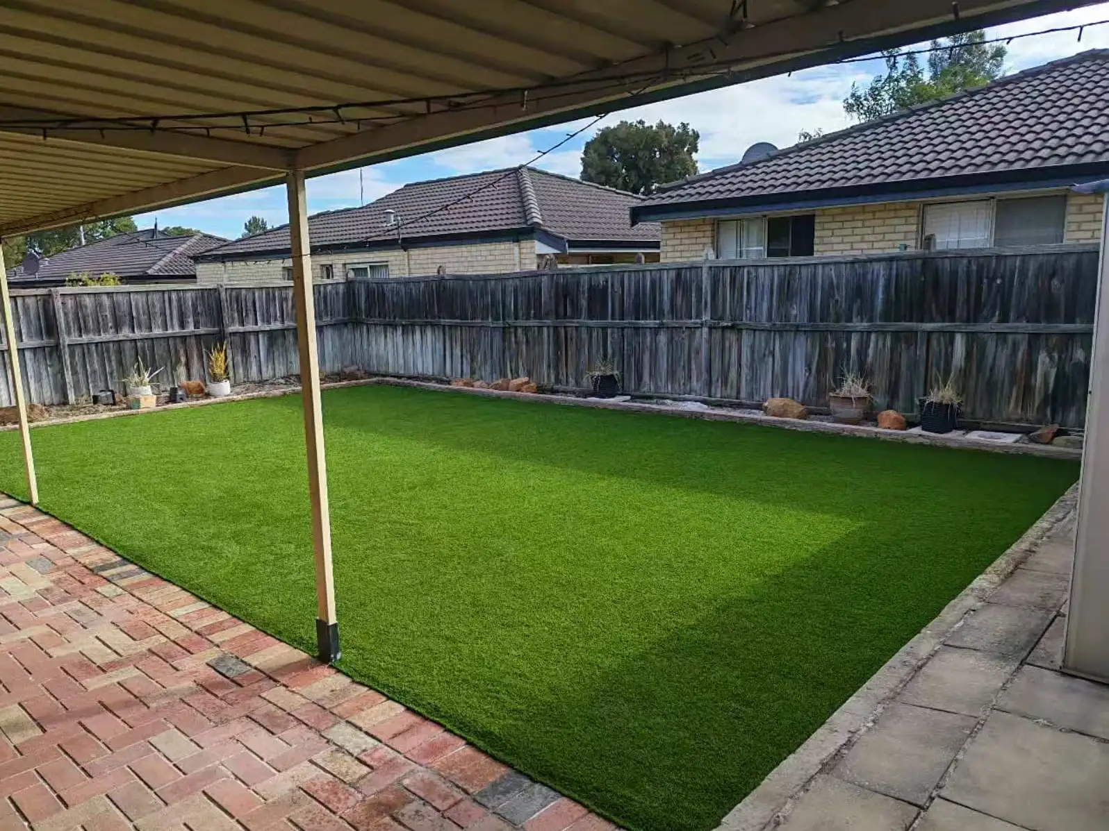 Backyard with a fresh artificial grass lawn and potted plants along the timber fence