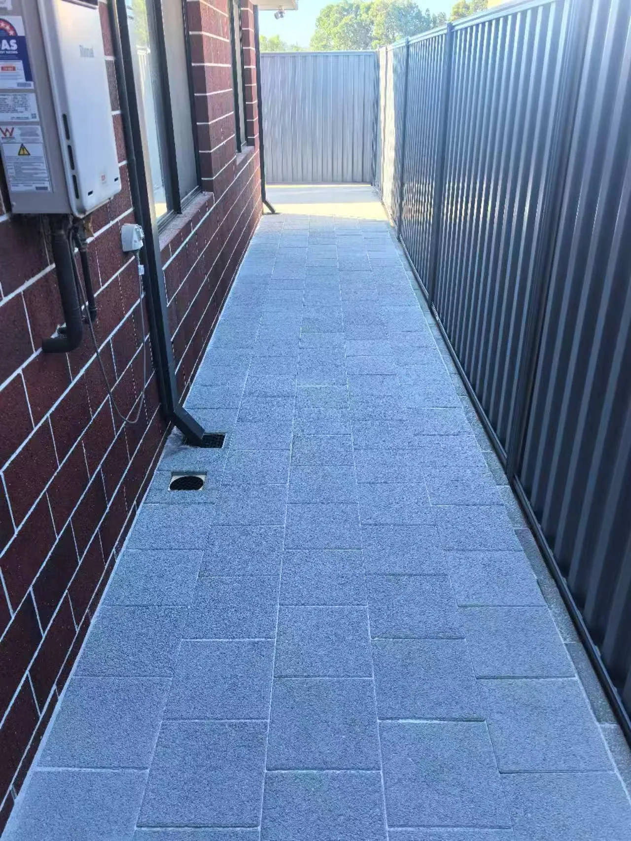 Side passage paved with grey granite-look pavers between a brick wall and a Colorbond fence